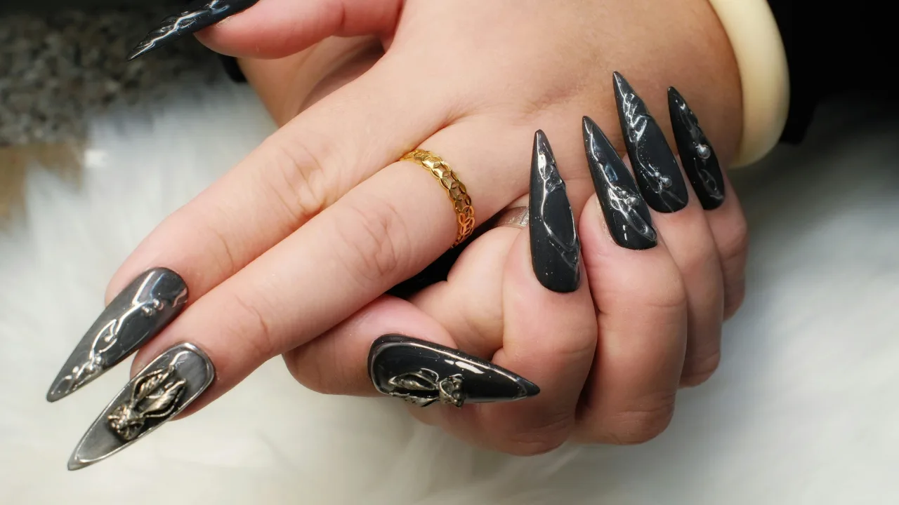 Long black stiletto nails with silver chrome nail art and a gold ring