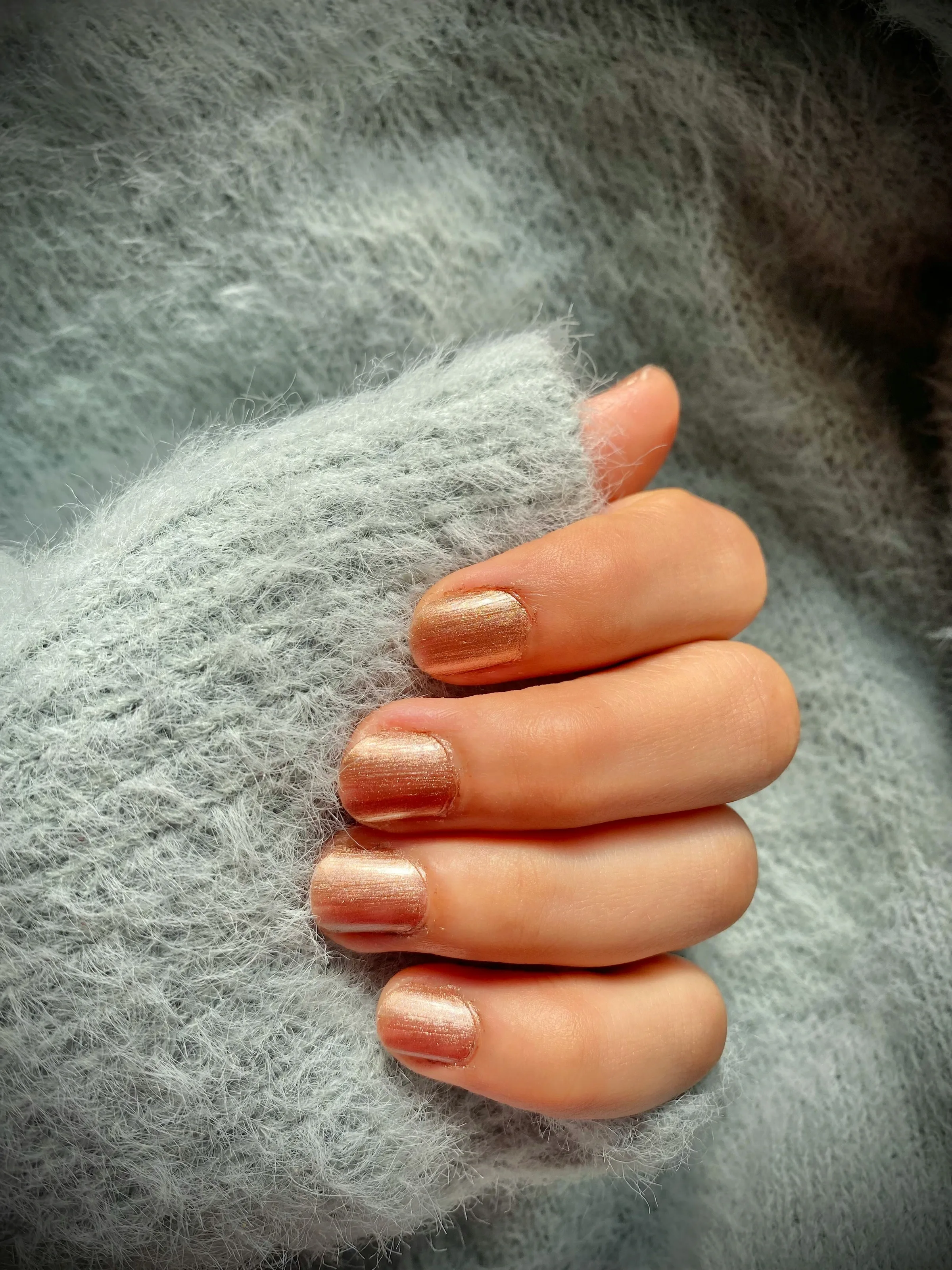 Short nails with a gold chrome gel finish against a soft grey knit
