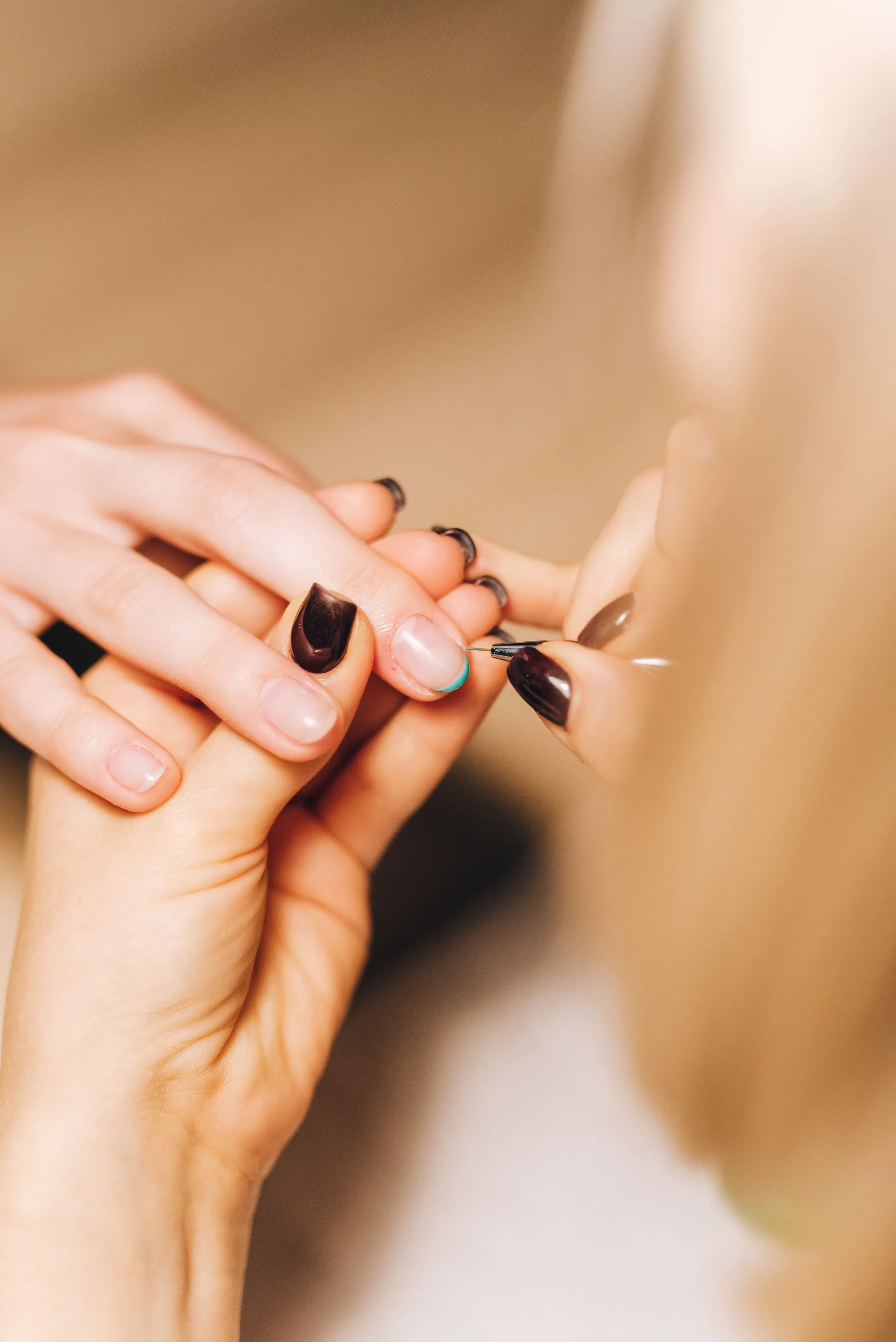 Nail technician painting a client's nails a deep plum shade