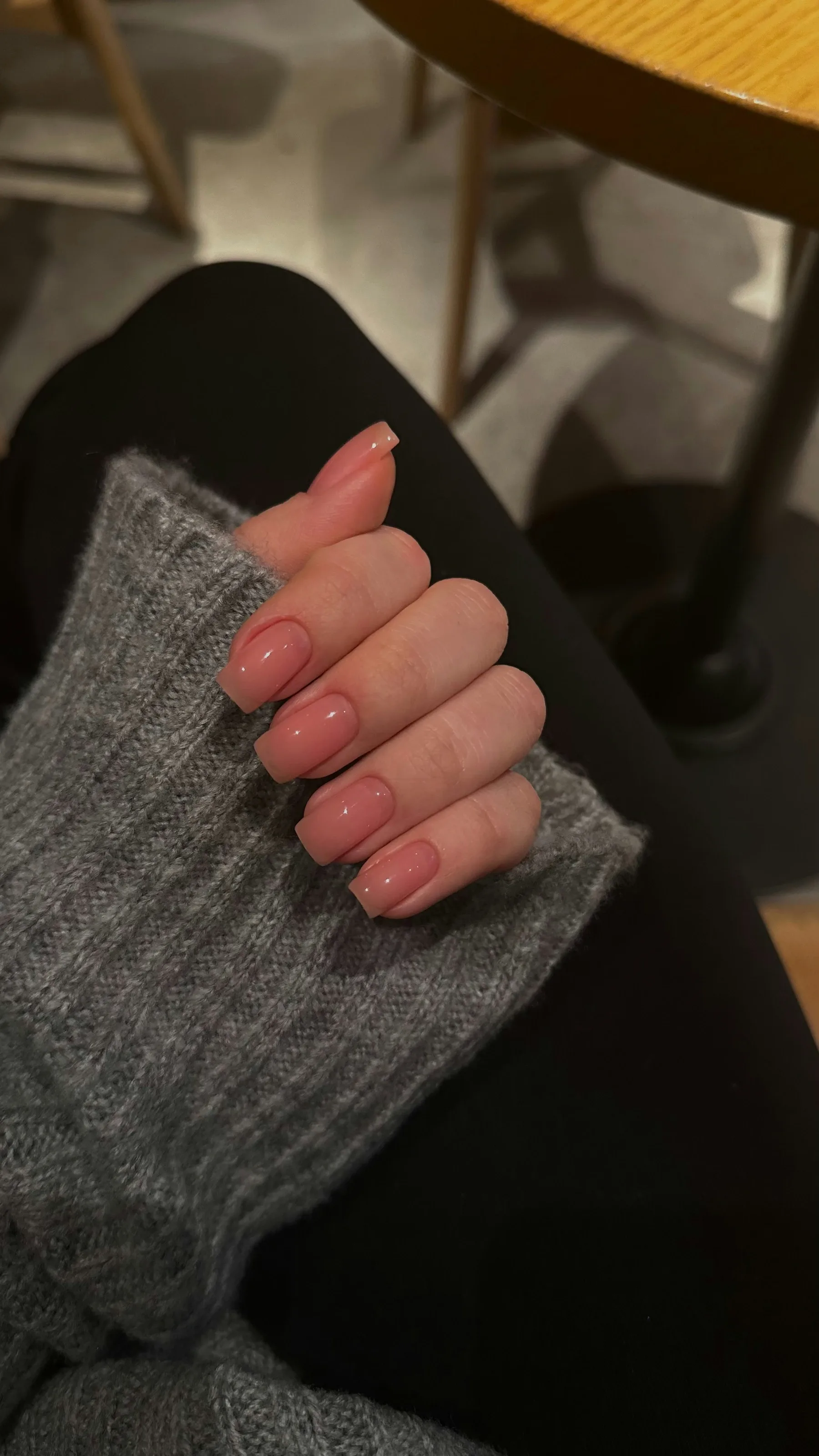 Hand with a glossy nude square manicure resting on a grey knit sleeve
